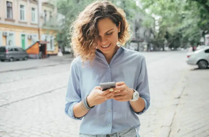 Uśmiechnięta kobieta na ulicy sprawdza telefon, być może szuka informacji o pożyczka kontomatik.