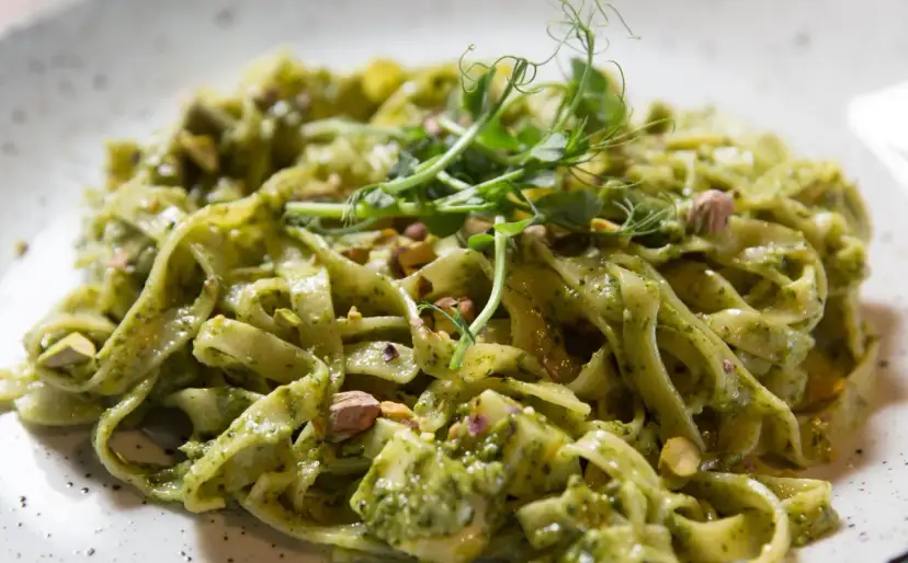 Makaron tagliatelle z zielonym sosem pesto, posypany pistacjami i udekorowany kiełkami.