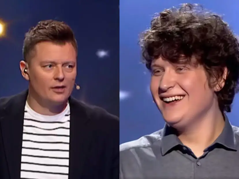Uśmiechnięty młody uczestnik i prowadzący w okularach na scenie programu "Jaka to melodia finał miesiąca".