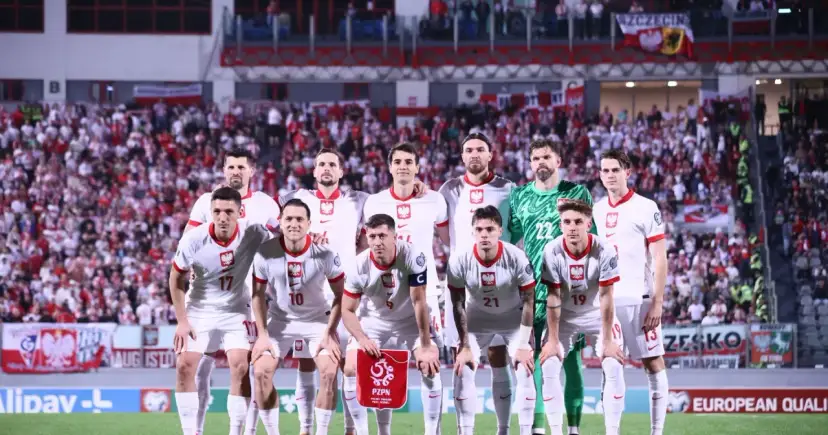 Piłkarze reprezentacji Polski w białych strojach, gotowi do gry. Tłum kibiców na trybunach, biało-czerwone barwy narodowe.