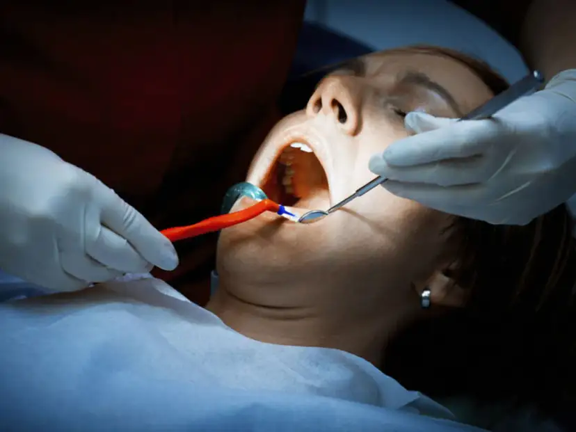 Dentysta bada usta pacjentki, która cierpi na ropień zęba. Widoczne narzędzia stomatologiczne i rozwierak.