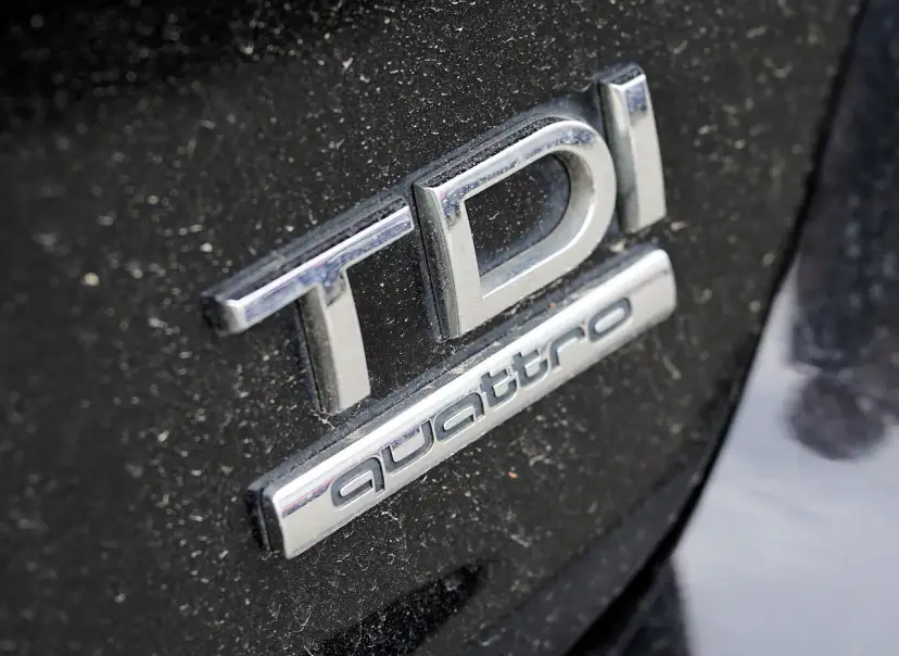 Emblematy TDI i Quattro na zakurzonym czarnym lakierze samochodu.