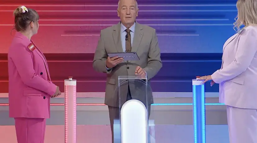 Prowadzący Familiady z tabliczką "Miliada" i dwie uczestniczki w różowych strojach. Zastanawiają się, co zmieniamy podczas jazdy samochodem.