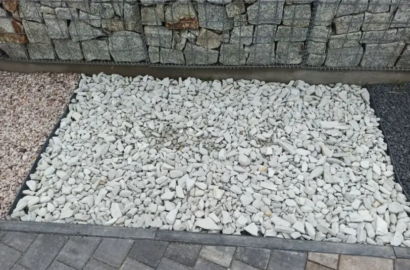 Biały grys na podjeździe obok gabionów i kostki brukowej.