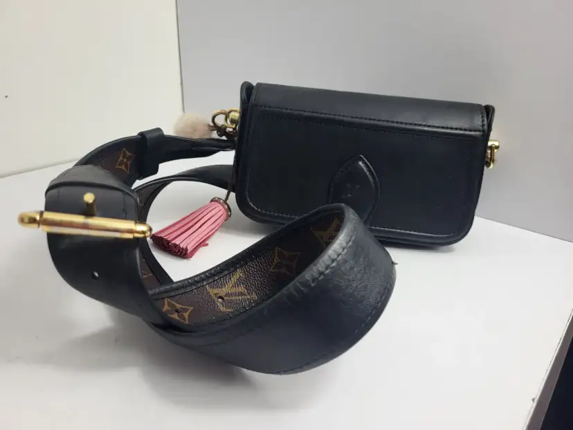 Elegancka, czarna louis vuitton torebka z ozdobnym, różowym pomponem i paskiem z monogramem.