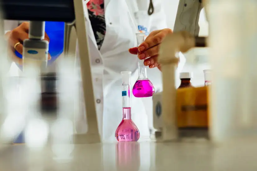 Ręce w białym fartuchu trzymające kolby z różowym płynem w laboratorium.