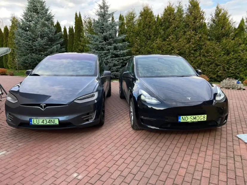 Dwa samochody Tesla, jeden ciemnoszary Model X, drugi czarny Model Y, stoją na podjeździe.