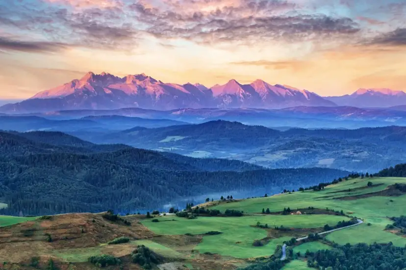 Tatry o zachodzie słońca, jedno z 5 najpiękniejszych miejsc w Polsce. Góry w odcieniach różu i fioletu, zalesione wzgórza i zielone pola.