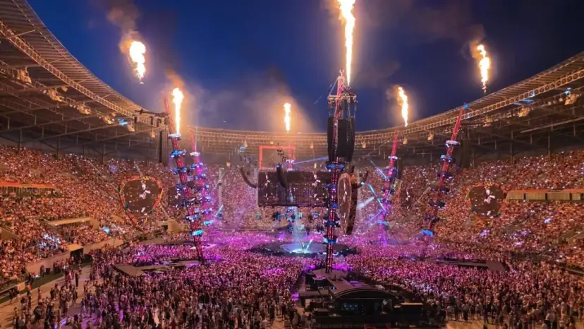 Koncert na stadionie z płomieniami, tłumem i sceną.