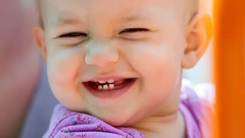 Uśmiechnięte dziecko z widocznymi ząbkami, które mogą być oznaką ząbkowania.