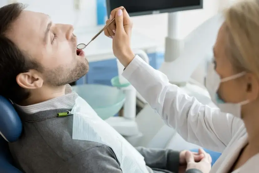 Pacjent u dentysty, zastanawia się, ile kosztuje wizyta u dentysty prywatnie. Lekarz bada jego zęby.