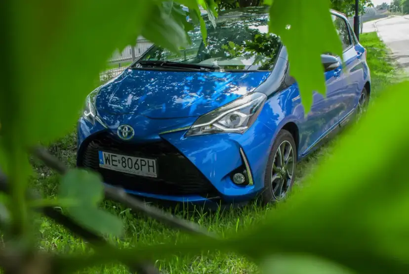 Niebieski Toyota Yaris Hybrid. Czy warto? Zobacz auto z bliska, ukryte wśród zieleni.