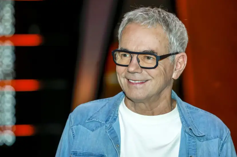 Uśmiechnięty mężczyzna w okularach, w jeansowej koszuli, jakby czekał na pytanie: "Jaka to melodia?".