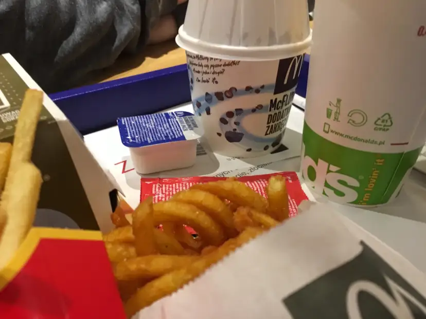 Zakręcone frytki McDonald's w pudełku z sosem i napojem.