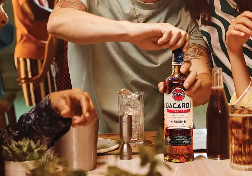 Osoba otwiera butelkę Bacardi Spiced obok szklanki z lodem i napoju.