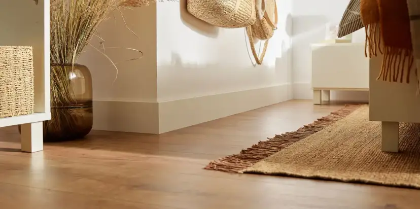 Widok na narożnik listwy przypodłogowej, drewnianą podłogę i dywanik.