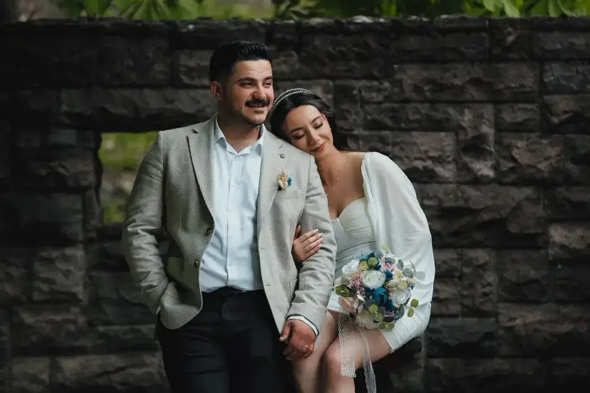 Para młoda w dniu ślubu, ona opiera głowę na jego ramieniu, trzyma bukiet.