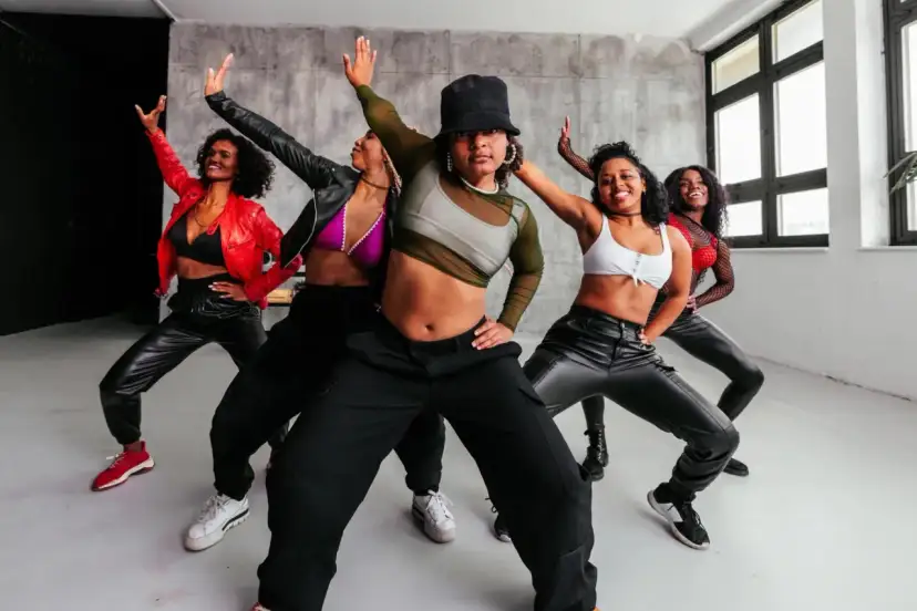 Pięć młodych kobiet w modnych strojach tańczy w studio. Różnorodne rodzaje tańca dla młodzieży, pełne energii i stylu.