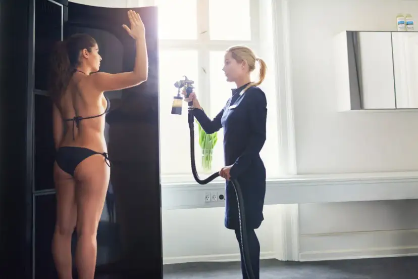 Kobieta w bikini przygotowuje się do opalania natryskowego. Czy po opalaniu natryskowym można się golić? Ekspertka trzyma pistolet do opalania.