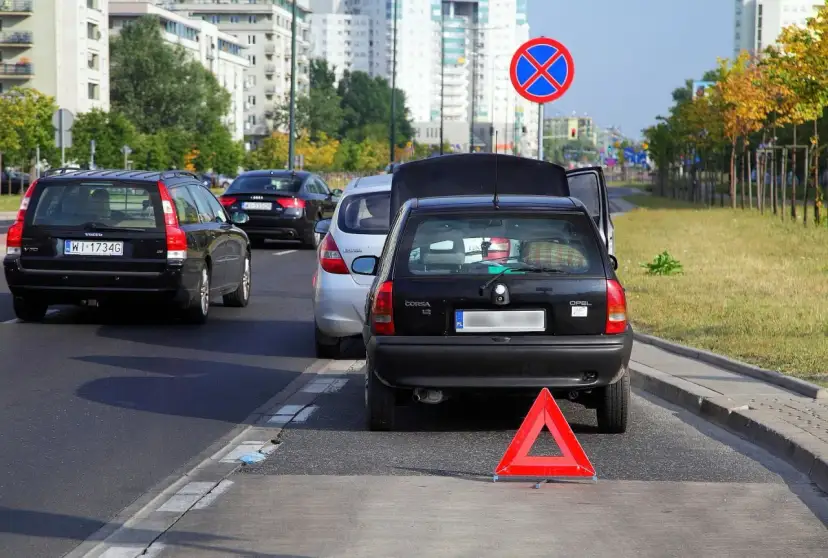 Czarny Opel z otwartą klapą bagażnika i trójkątem ostrzegawczym na autostradzie.