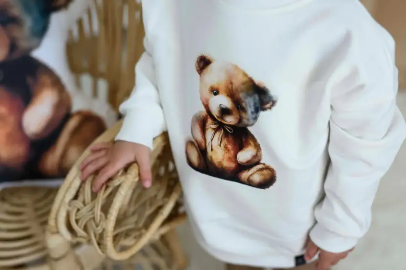Biała bluza Moschino z uroczym misiem w stylu vintage. Dziecko trzyma się wiklinowego koszyka.