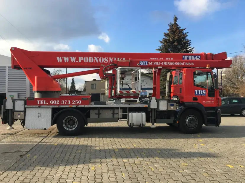 Czerwony podnośnik koszowy WUMAG WT 450 z koszem roboczym i wysięgnikiem. Na pojeździe widnieje napis WWW.PODNOSNIKI-TDS.PL.