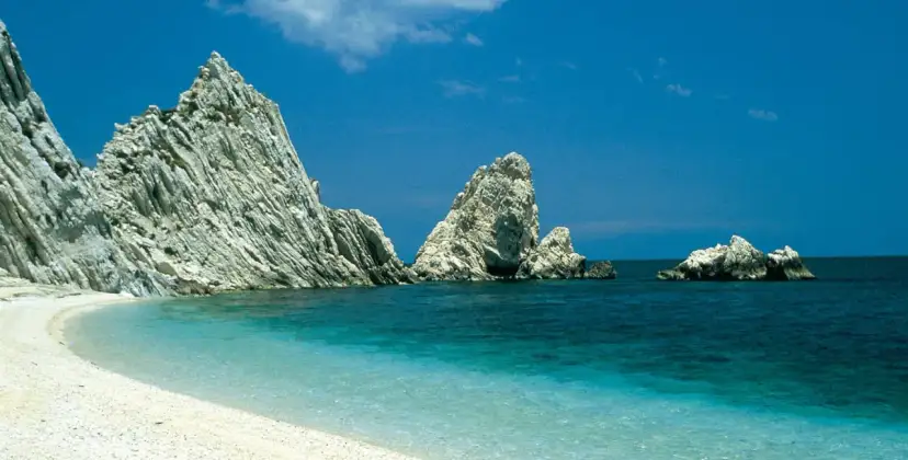 White pebble beach with turquoise water and dramatic white rock formations under a clear blue sky.