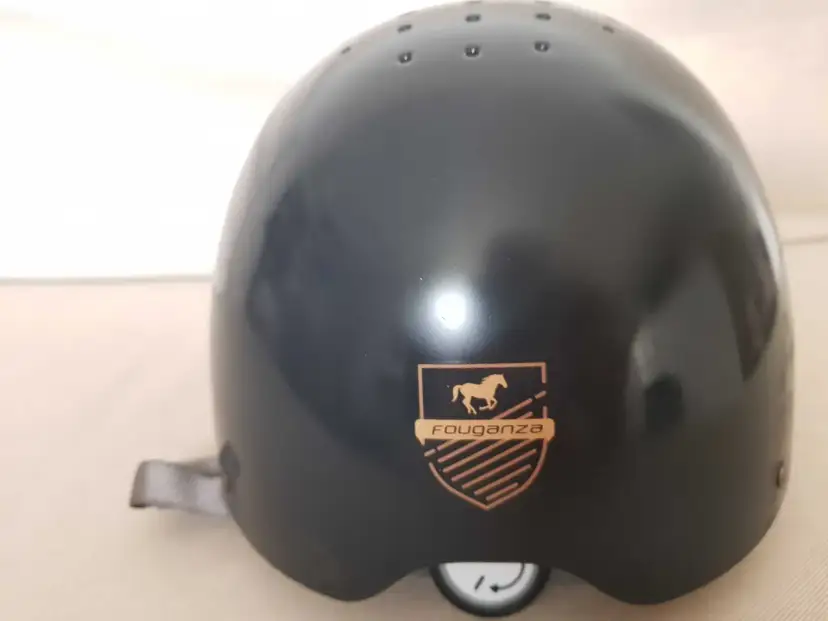 Czarny kask jeździecki Fouganza z logo konia i tarczą.