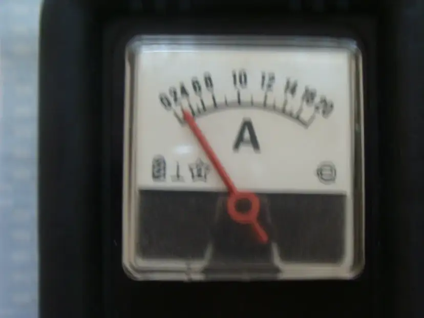Zbliżenie na analogowy wskaźnik amperomierza z czerwoną wskazówką.